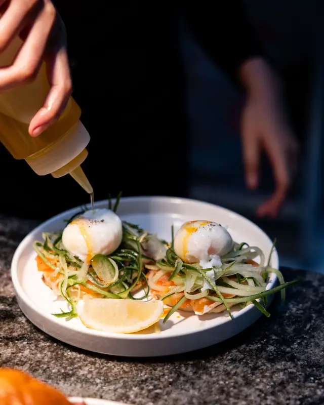 A chef finishes two poached eggs with a squeeze bottle.
