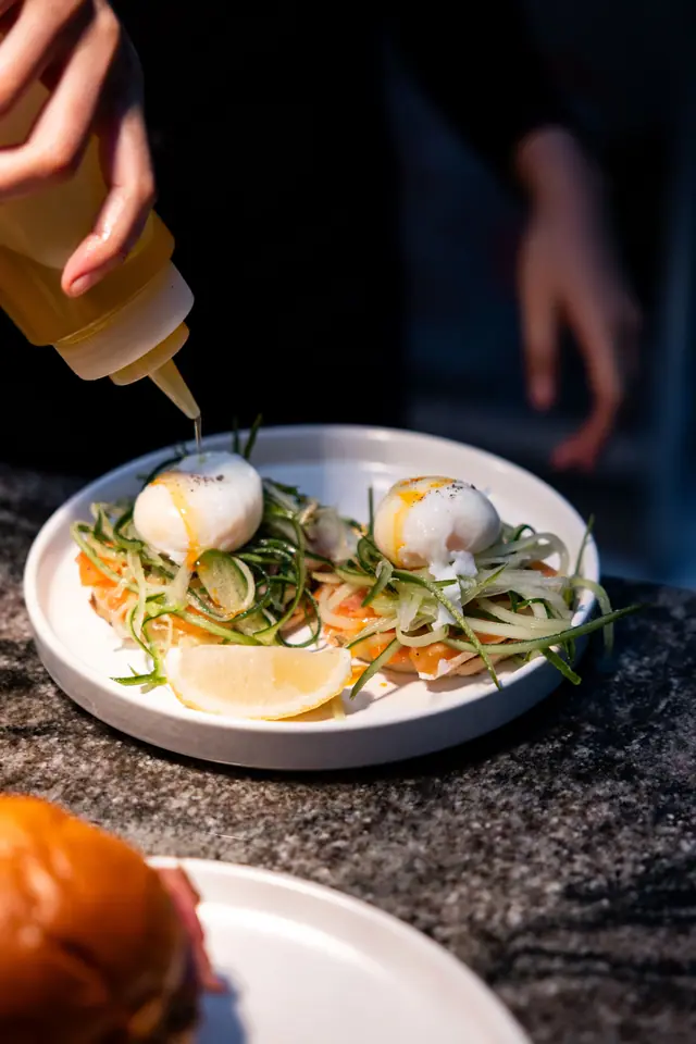 Un chef termine deux œufs pochés avec un flacon de sauce.