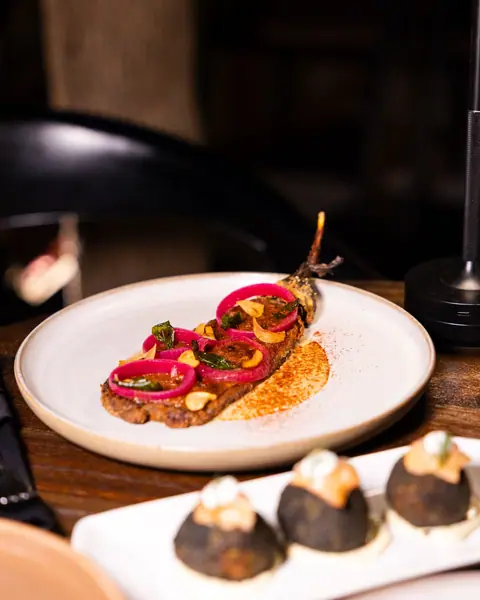 A crispy aubergine cutlet with pickled onion on a round plate.