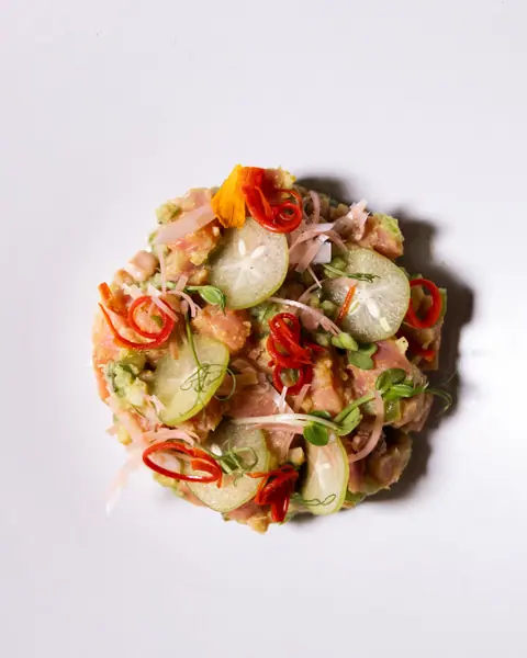 Tuna ceviche with slices of star fruit and red chilli on a white plate.