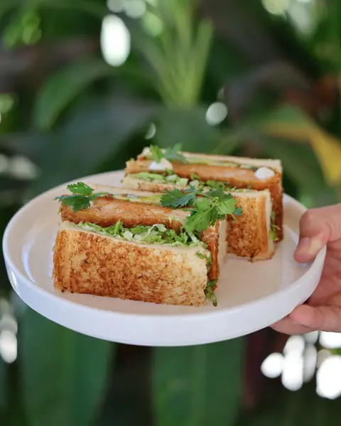 A chicken katsu sando cut in three, held up in the garden.