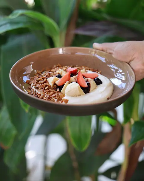 A bowl of Greek yogurt with granola, banana, strawberry and berry compote.