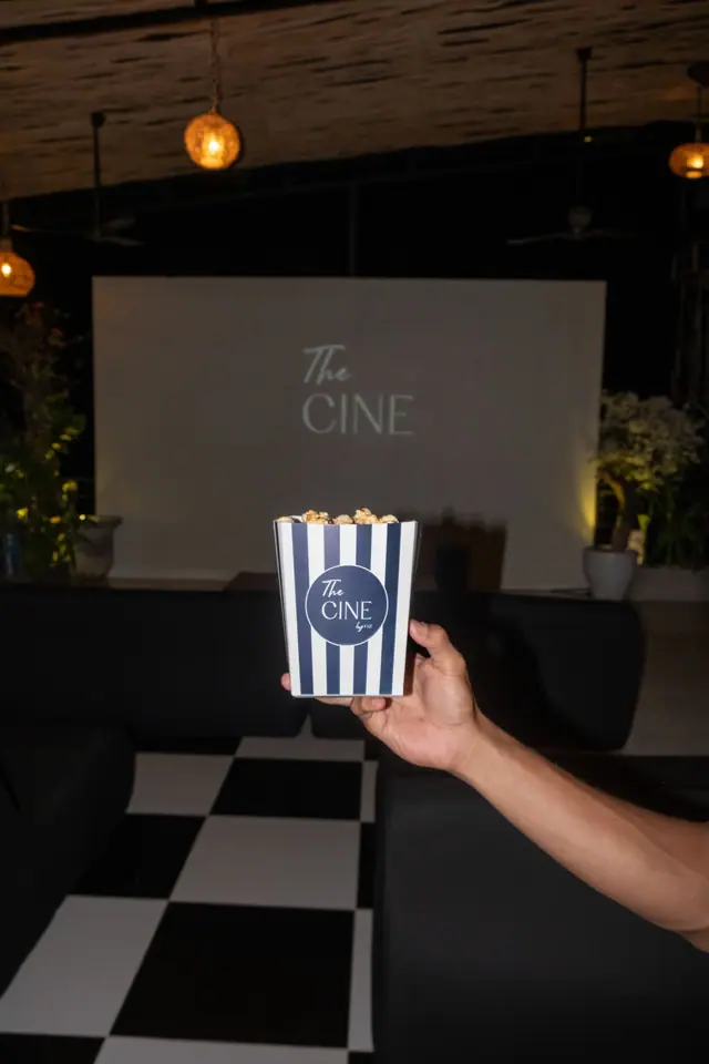 Une main tient une boîte de pop-corn rayée devant l’écran de cinéma.