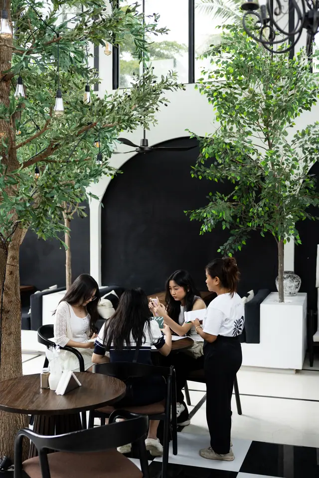 Des amies autour d’une table sous les arbres, une serveuse prend la commande.
