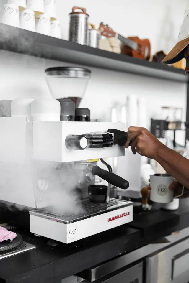 Un barista à la machine à espresso blanche, dans la vapeur.