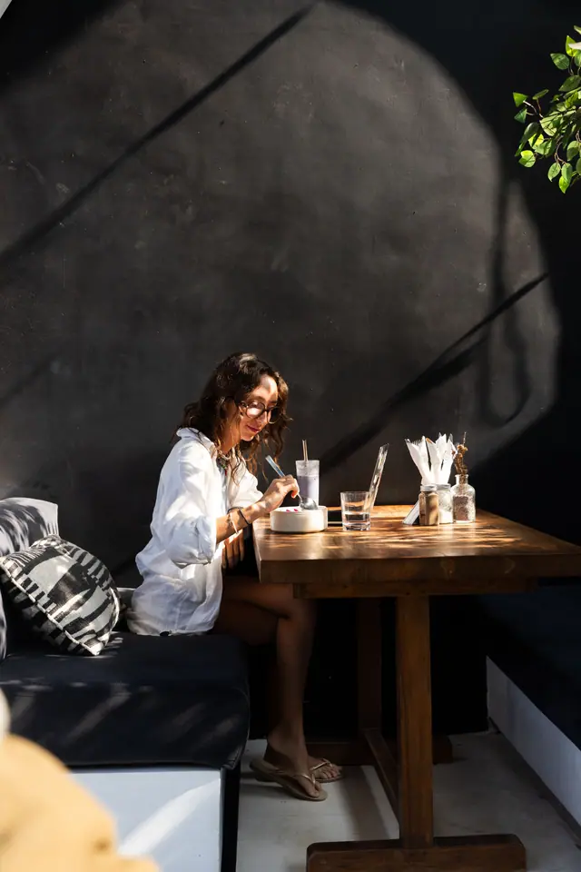 Une cliente prend son petit-déjeuner sous une arche noire, au soleil du matin.