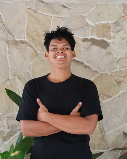 Sanu in front of a stone wall, arms crossed, smiling.