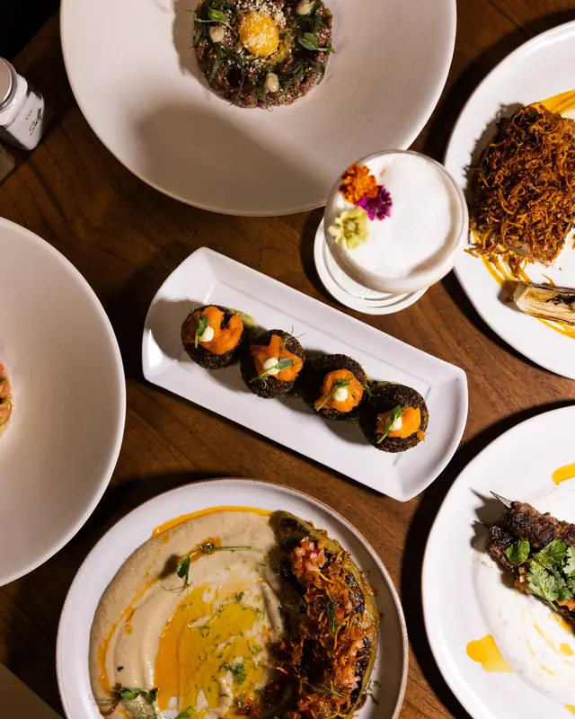 Meja makan malam dilihat dari atas: mezze, arancini, dan tartare di piring putih.
