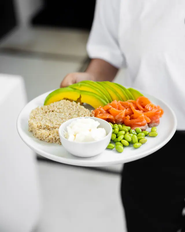 Piring racikan sendiri sedang diantar ke meja: quinoa, salmon asap, alpukat, dan edamame.